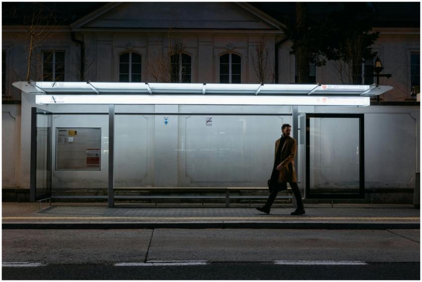 A man walks past a lit bus stop at night, creating