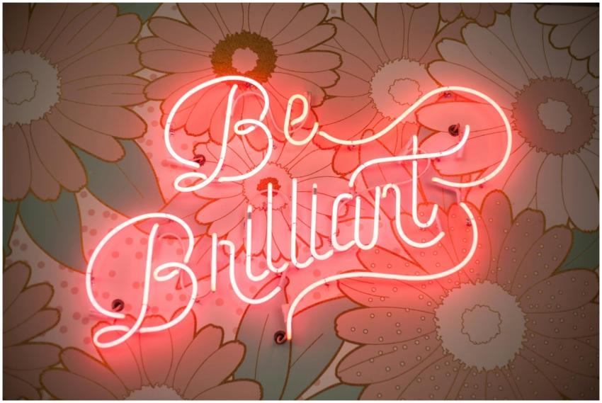 A glowing neon sign reading 'Be Brilliant' against