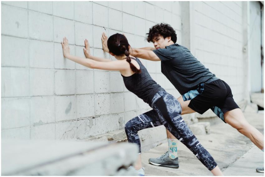 Man and woman stretching against a wall outdoors,
