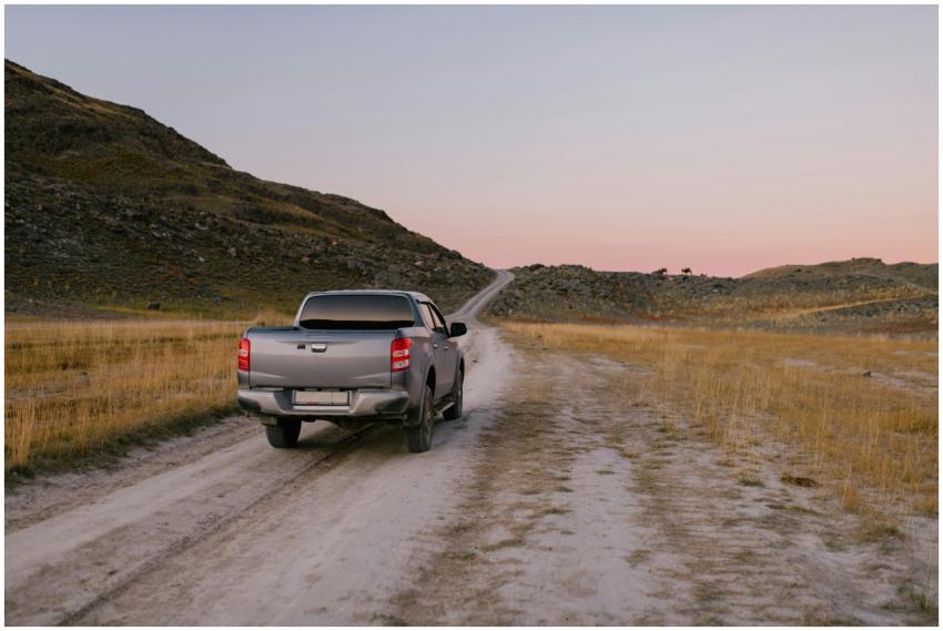 A pickup truck travels down a dusty rural road at