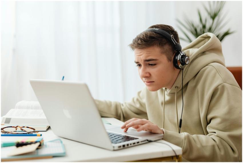 Teen wearing headphones studies online with a lapt