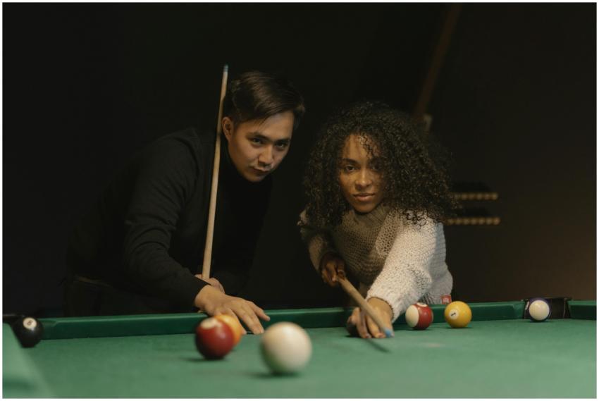 Two adults playing billiards indoors, focusing on