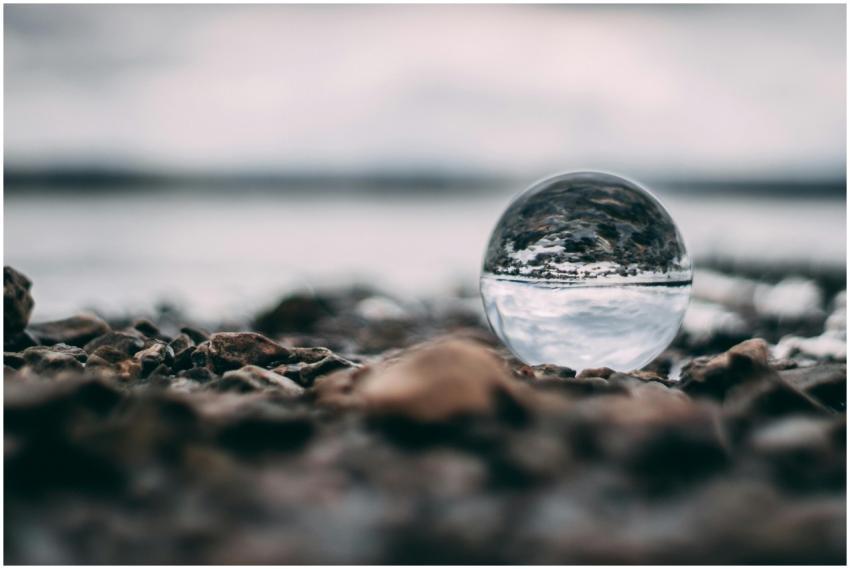 A glass sphere on a rocky beach capturing an inver