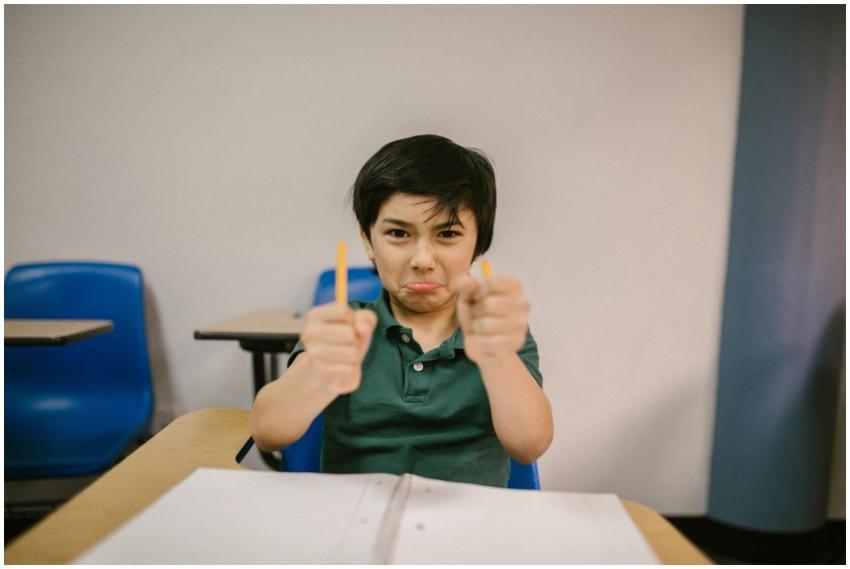 A young boy in a classroom showing frustration, ho