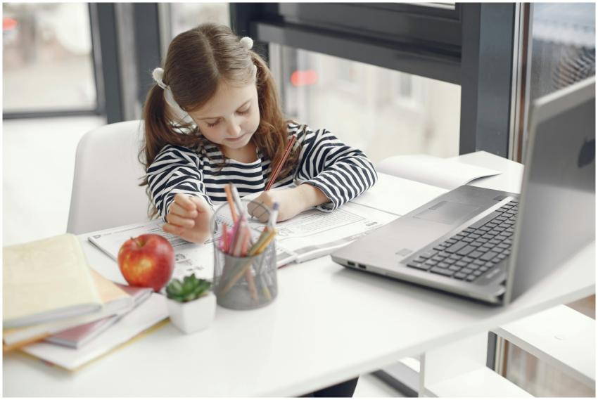 A young girl studies at home using a laptop, engag