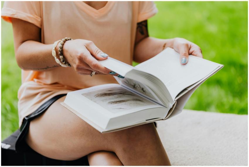 Woman sitting outdoors reading a book, wearing a p
