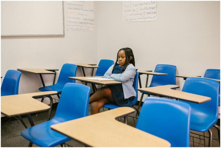 A young girl sits alone in a classroom, depicting