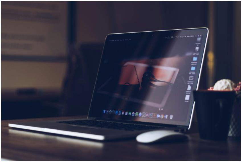 A sleek laptop on a wooden desk with a cup, creati