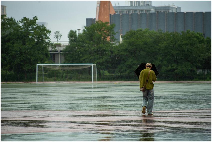 A solitary figure with an umbrella walks on a wet