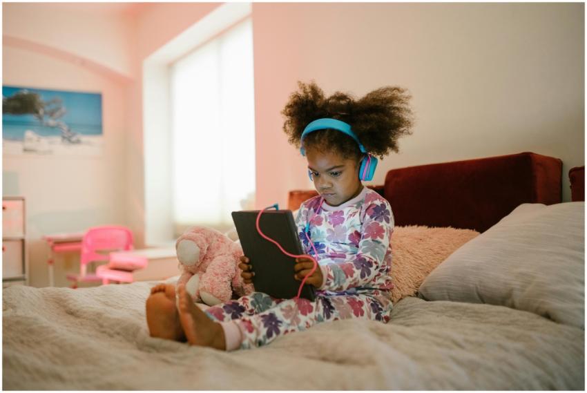 A young girl in pajamas sits on the bed with headp