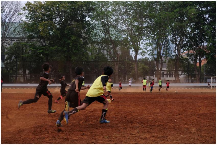 Group of kids playing soccer on a dirt field with
