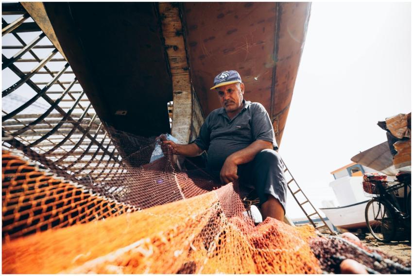Fisherman repairs a net under a boat in Damietta,