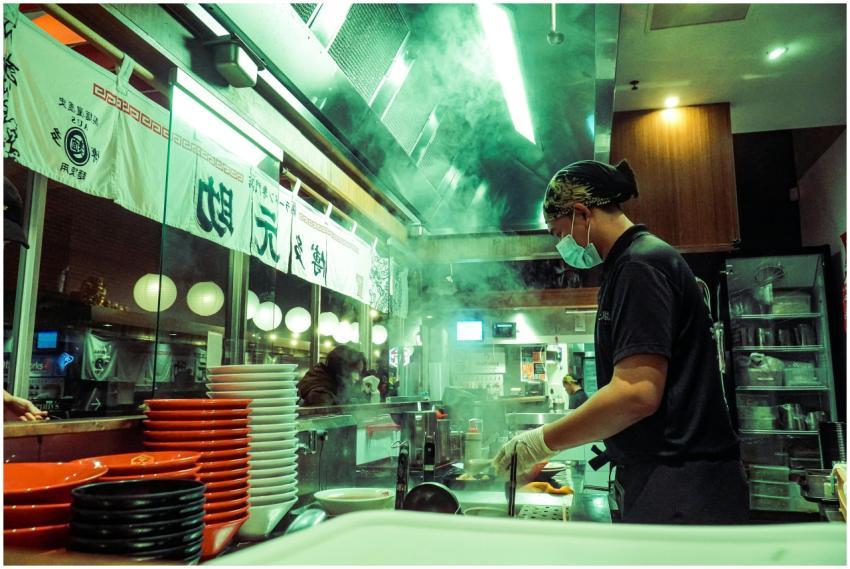Masked chef prepares food in a bustling Asian rest