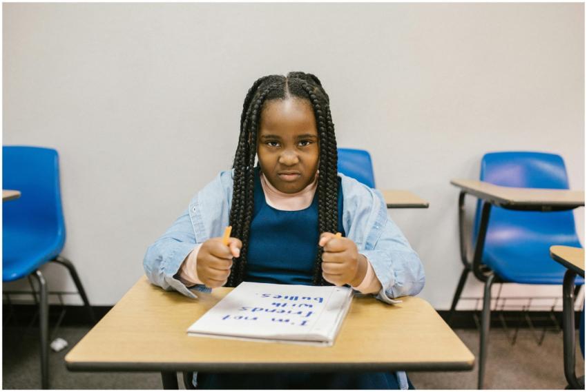 A young girl sits at a desk with a determined expr
