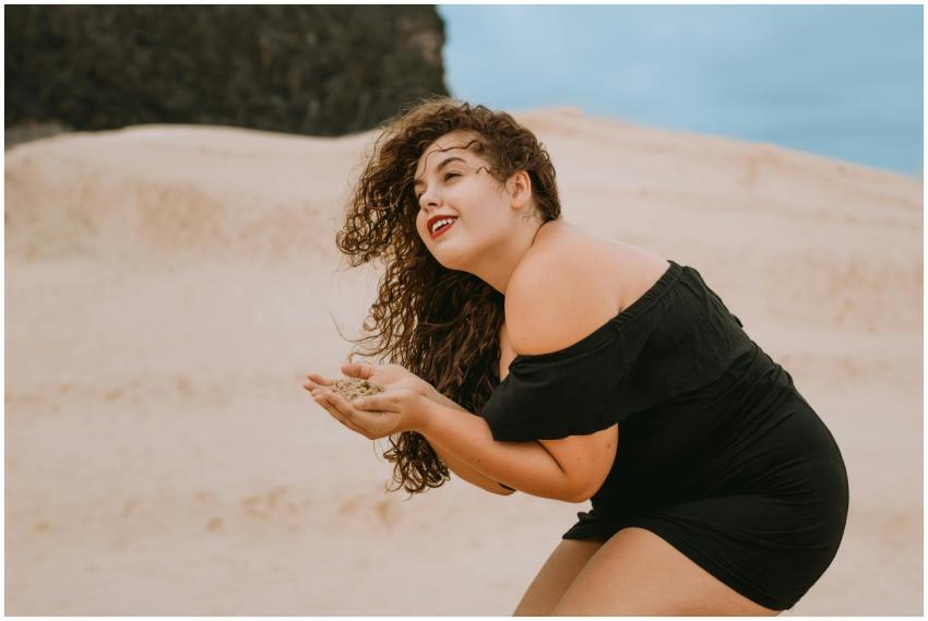 Woman in a black dress at the beach enjoying sand.