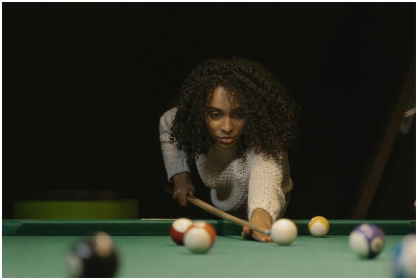 Focused woman with curly hair aiming a cue ball on