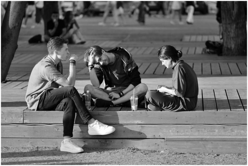 Three young adults sitting on a bench chatting in