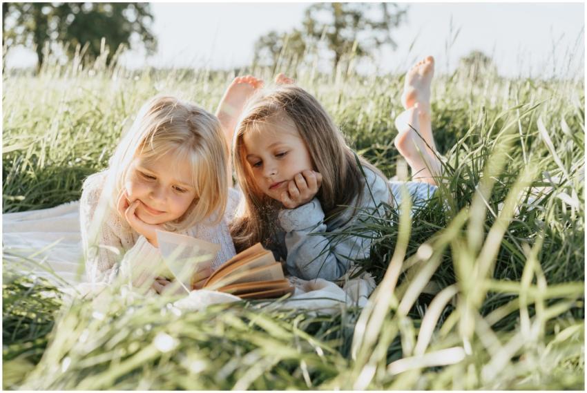 Two young girls lying in a grassy field reading a