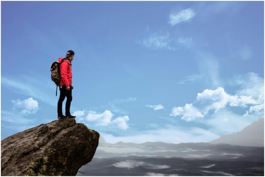 Hiker in red jacket stands on a cliff edge, overlo