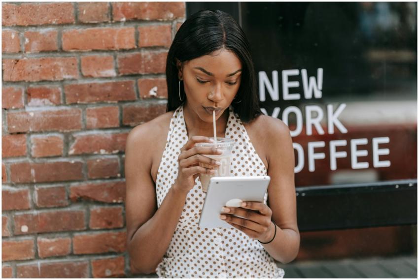 Woman sipping iced coffee and using a tablet outsi