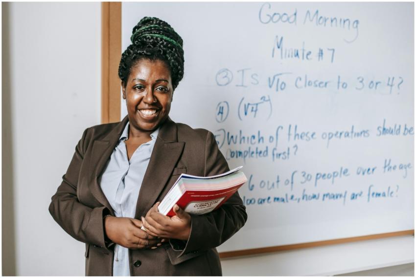 A smiling teacher holding textbooks stands confide