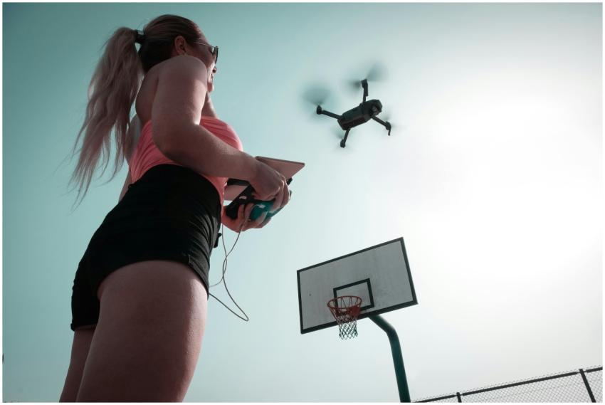 A woman operates a drone near a basketball court,