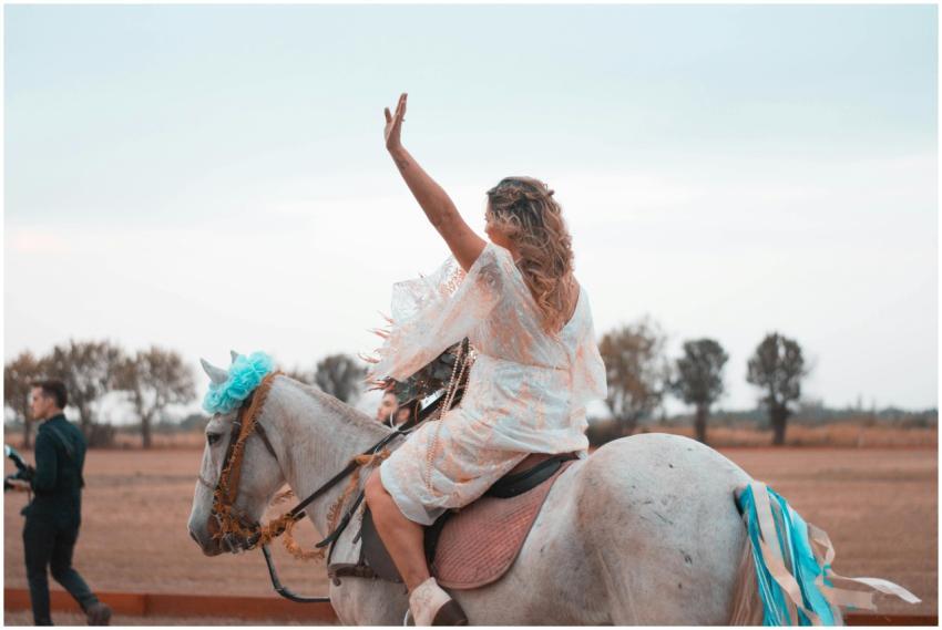 Woman riding a decorated white horse, waving amids