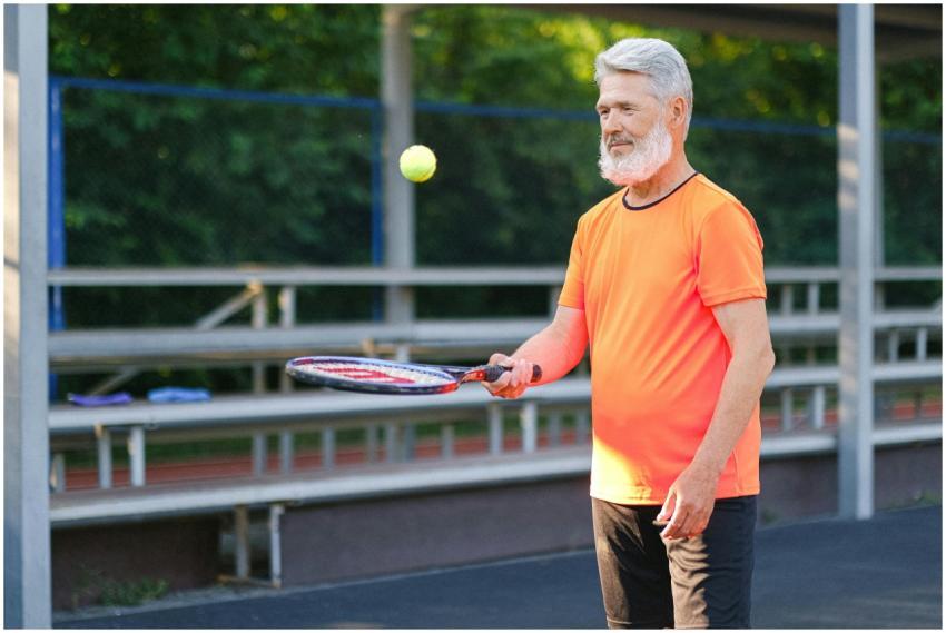 Elderly man in bright sportswear playing tennis ou
