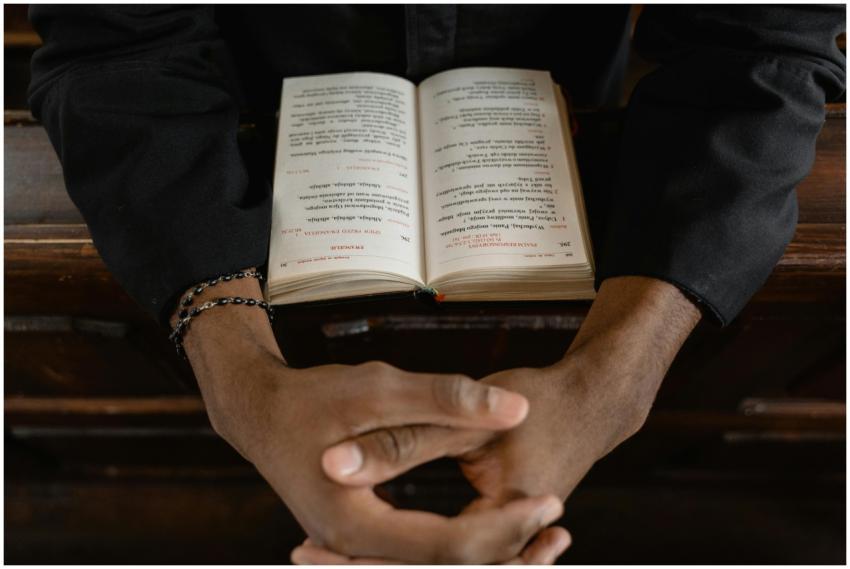 Close-up of hands clasped over an open Bible, symb