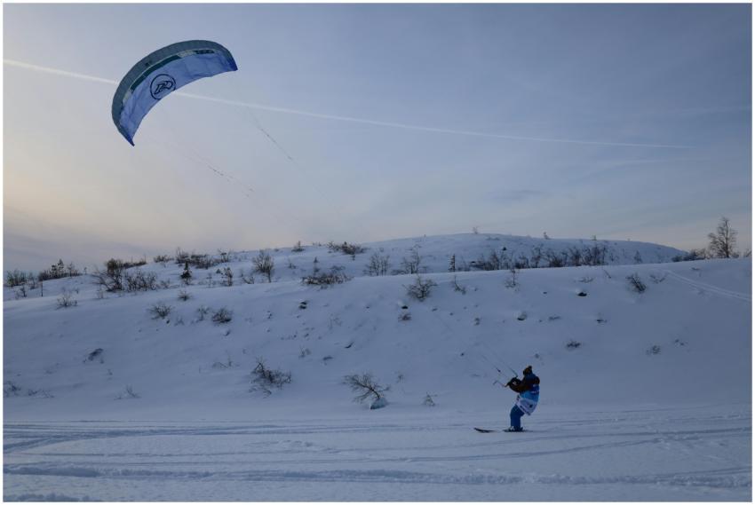 A person kiteboarding on snowy terrain in Kirovsk,