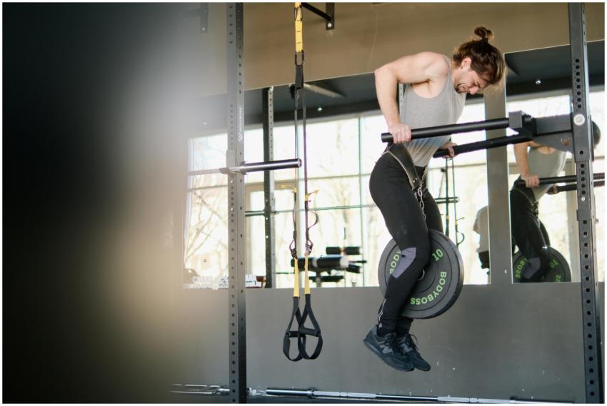 Fit man performing weighted pull-ups in a gym sett