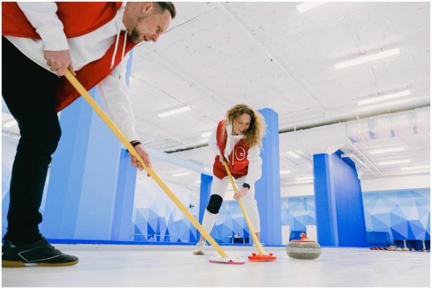 Two athletes practicing curling indoors with focus