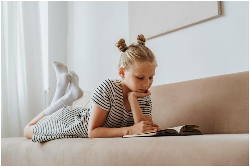 Young girl enjoying a book while lying on a couch,