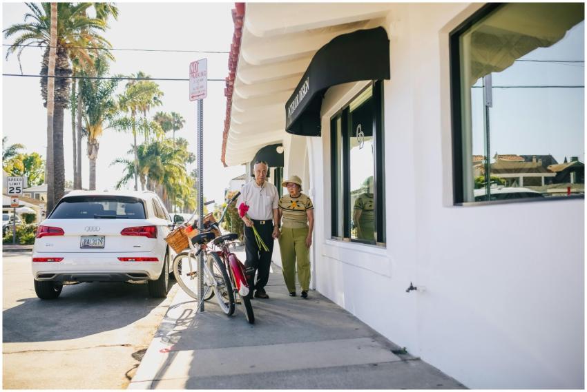 An elderly couple walks hand in hand outside a sho