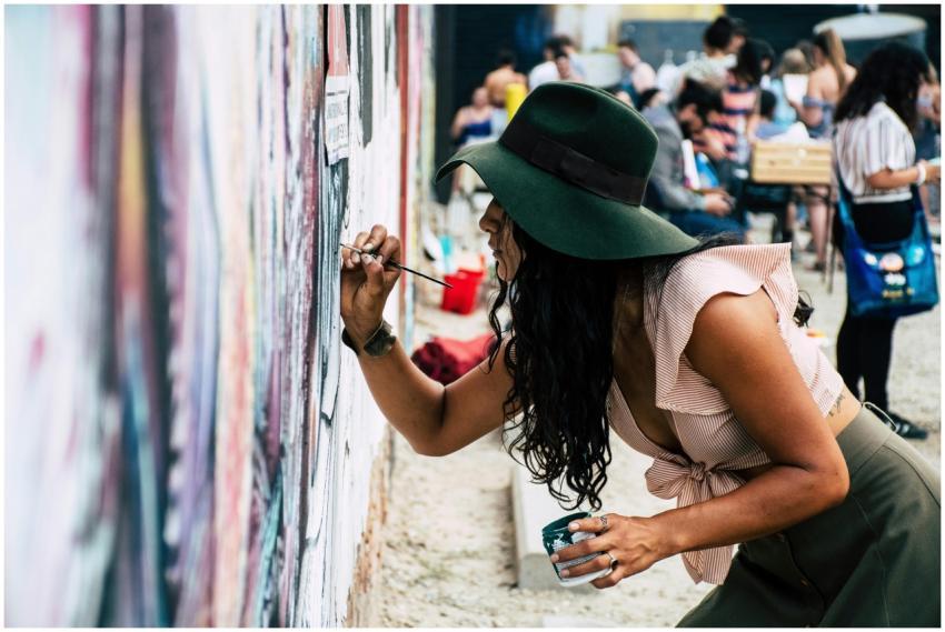 Young woman wearing hat painting a mural on an urb