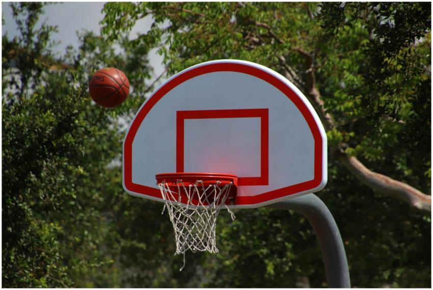 Basketball hoop with ball in mid-air on a sunny ou