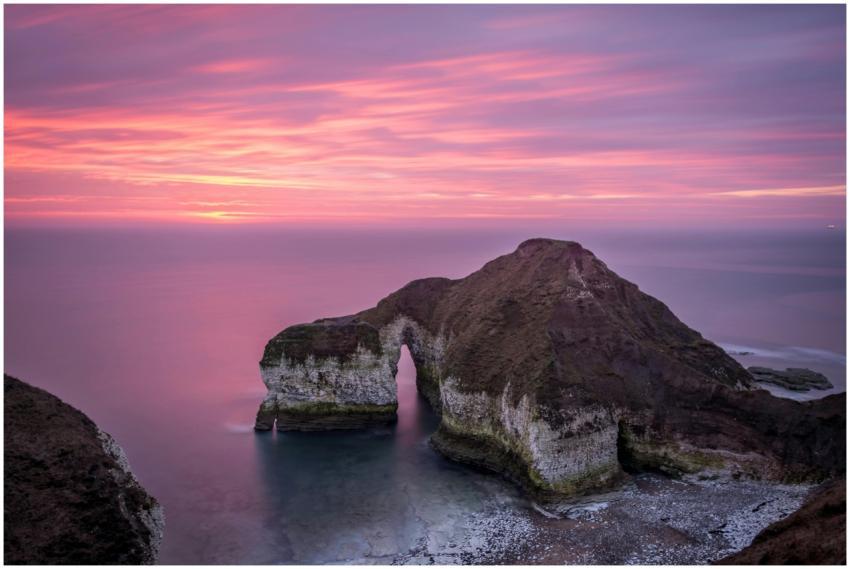 Serene seascape featuring a natural arch at sunset