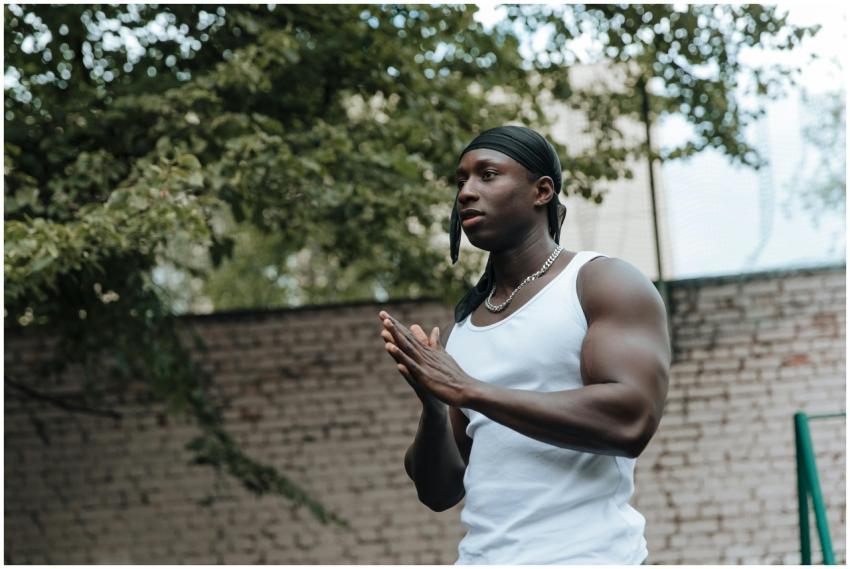 Muscular man standing outdoors with hands folded,