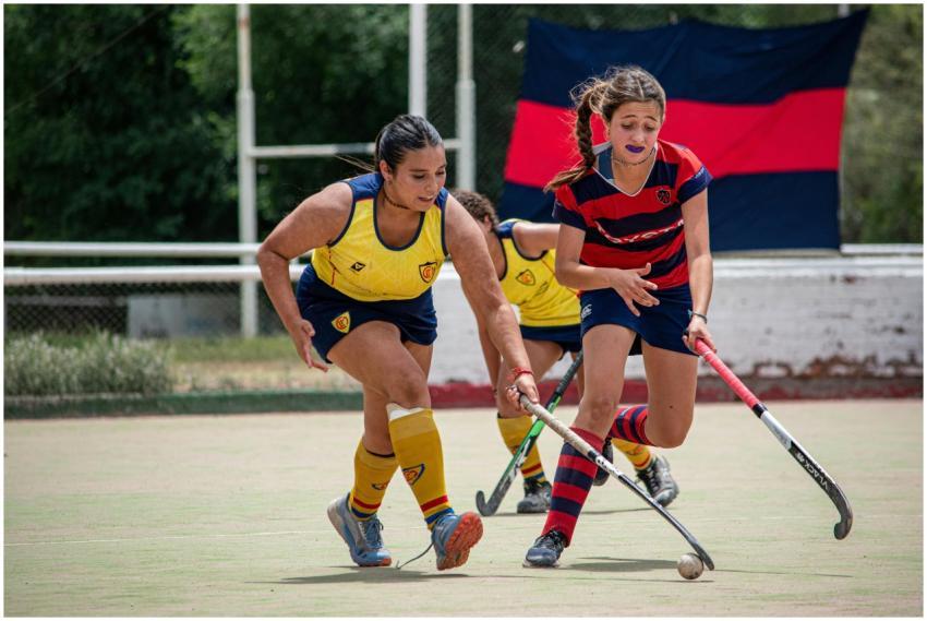 Two women playing field hockey outdoors, showcasin