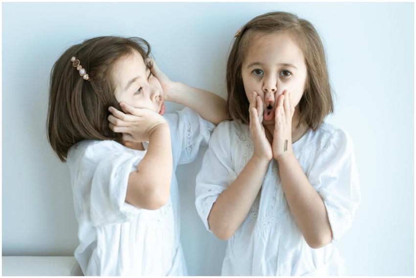 Two young girls in white dresses express playful e