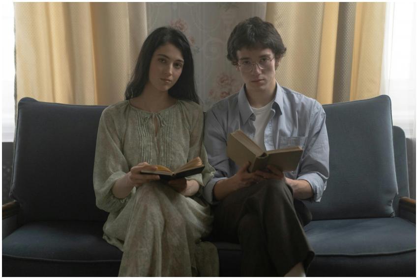 A young couple sits on a couch indoors, each holdi