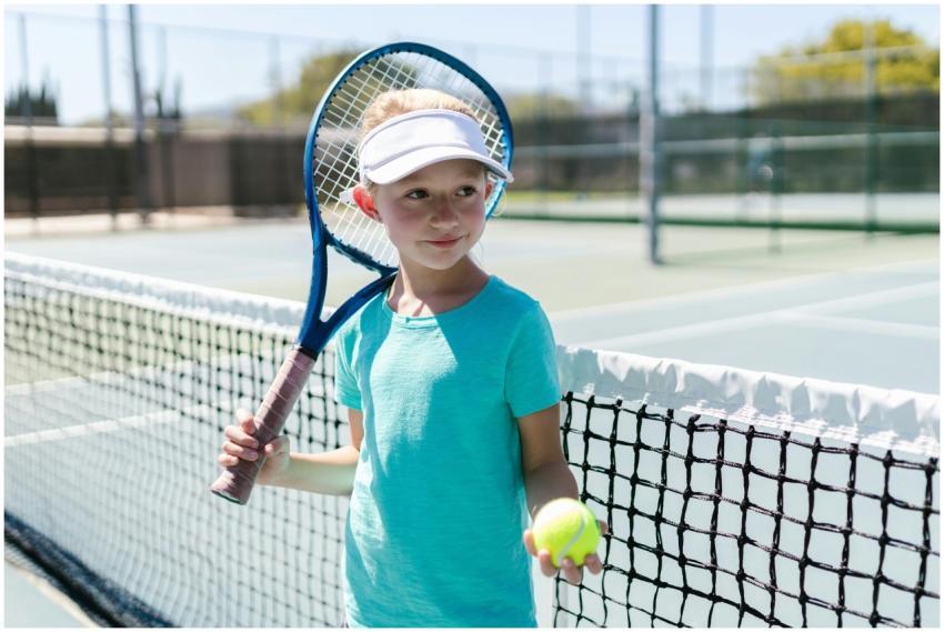 Smiling girl holding tennis racket and ball on an
