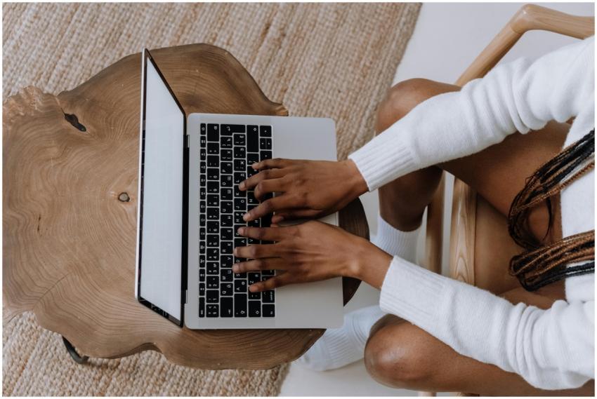 A woman typing on a laptop at a stylish wooden tab