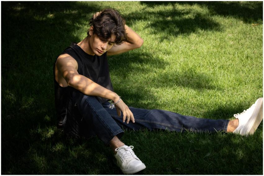 A young man in casual attire sits thoughtfully on