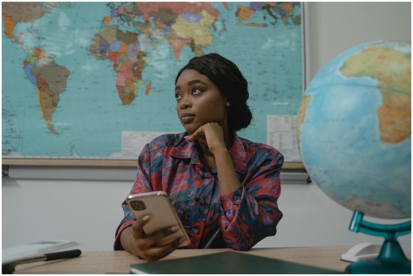 A teacher in a classroom, pondering with a smartph
