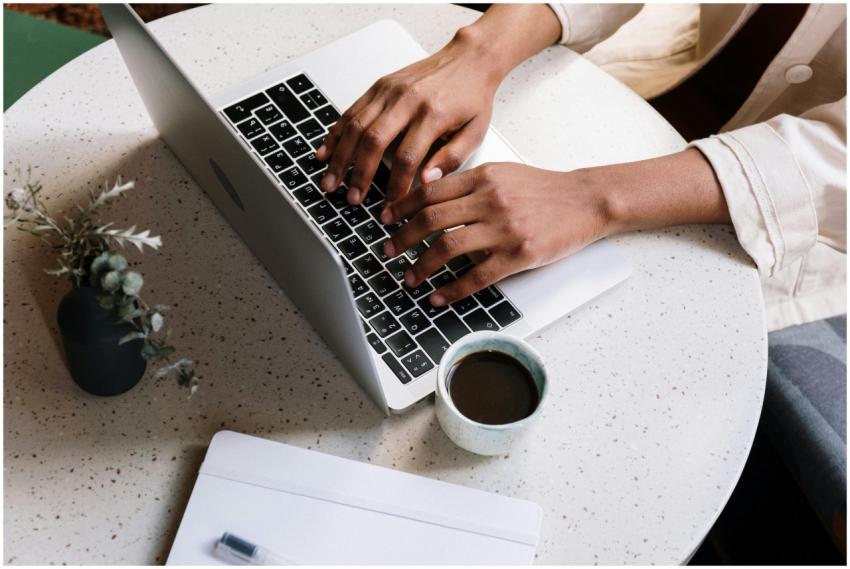 A person typing on a laptop at a café table with c