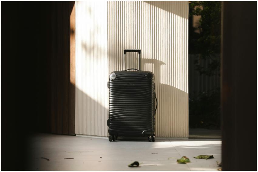 A sleek black suitcase stands in a sunlit hallway,