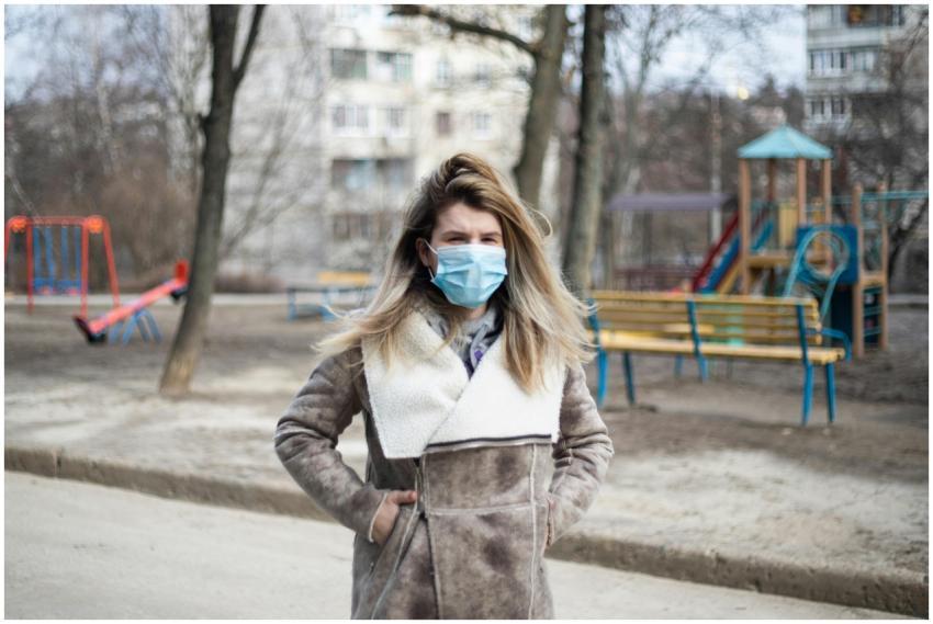 A woman in a coat and face mask stands in an urban