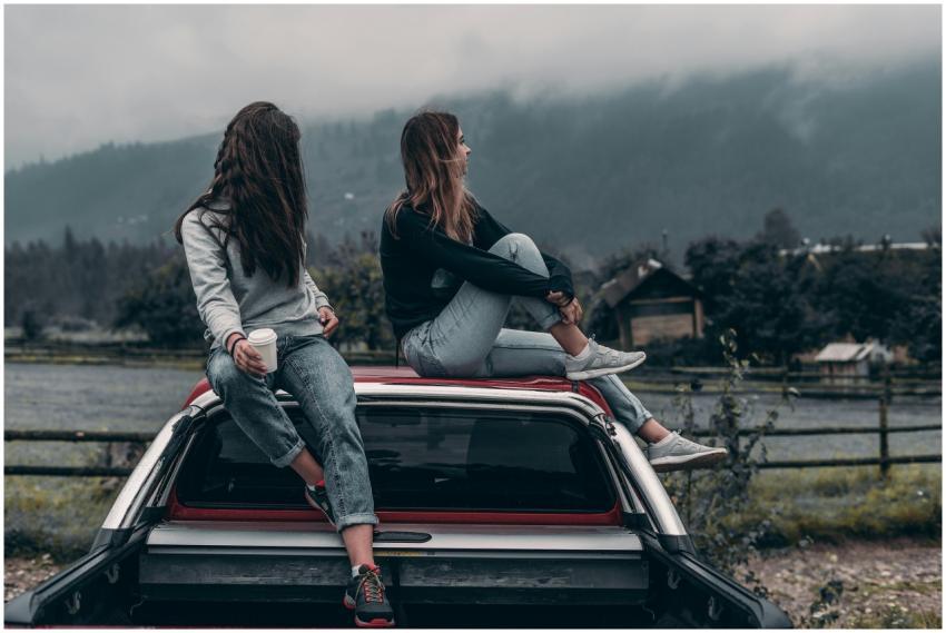 Two young women sitting on a car, enjoying the ser