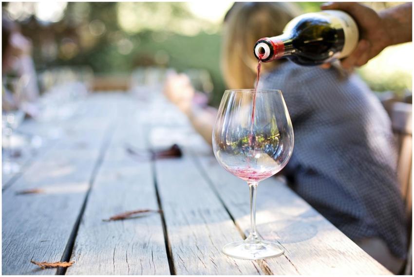 A hand pouring red wine into a glass on an outdoor
